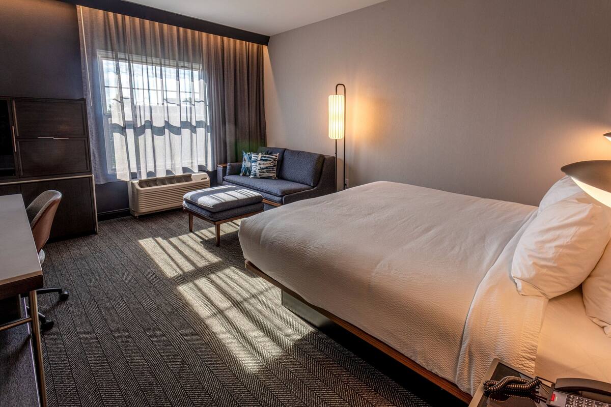 A hotel room with a large bed, a desk, a chair, a sofa, and a standing lamp.