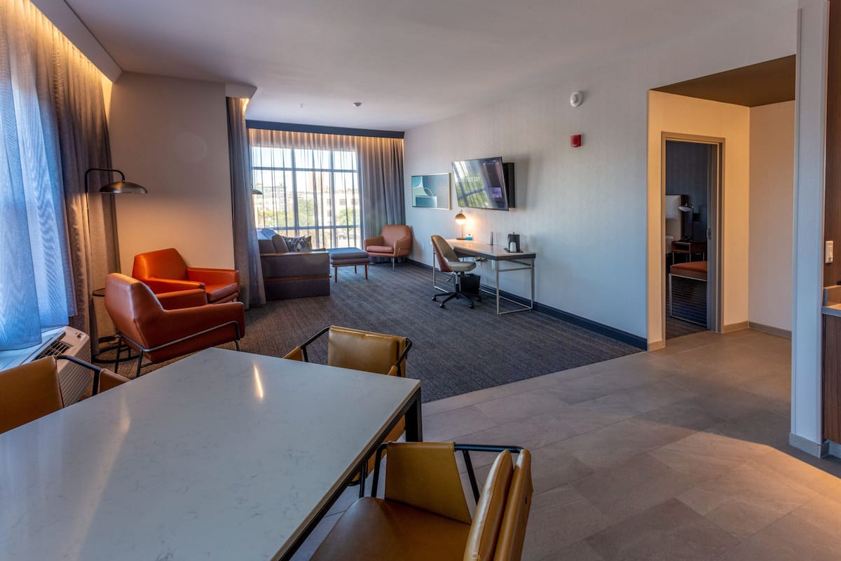 A hotel room with a dining area, a sofa, a desk, and a TV.
