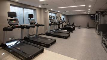 Une salle de sport équipée de plusieurs tapis de course, d’appareils de musculation et d’un écran de télévision.