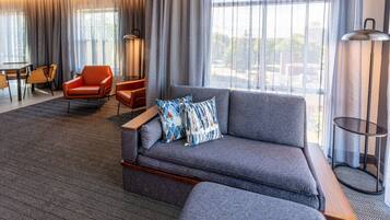 Une chambre d’hôtel moderne avec un canapé gris, un fauteuil orange et un coin repas comprenant une table et des chaises.