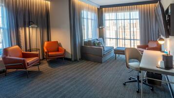 A hotel room with a sofa, two armchairs, a desk, and a television.