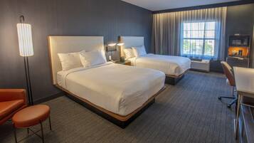 A hotel room with two beds, a desk, a chair, a lamp, and a TV.
