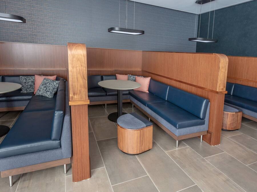 A modern lounge area with seating arrangements, including a long bench, a round table, and a small stool.