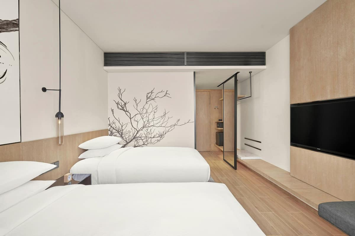 Quarto de hotel moderno com uma cama grande, televisão de tela plana, armário de madeira e espelho.