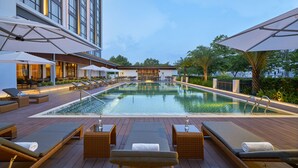 A rooftop pool area with lounge chairs, umbrellas, and a view of the city skyline.