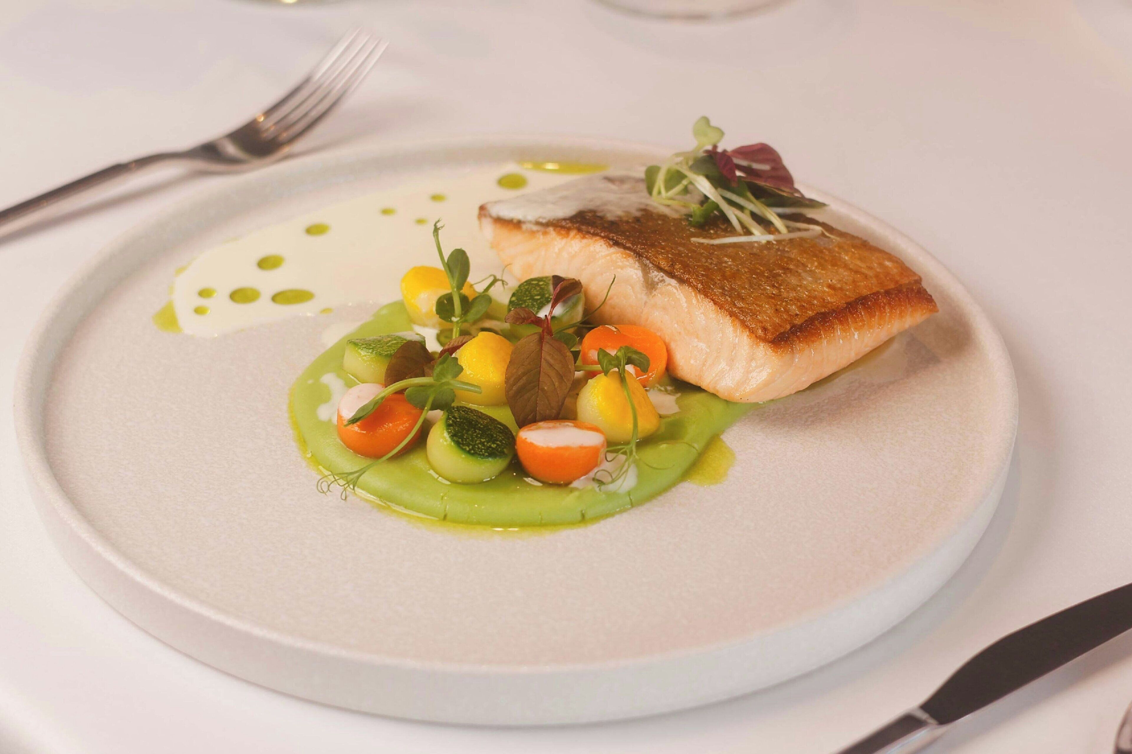Um prato com um pedaço de peixe, legumes e molho.