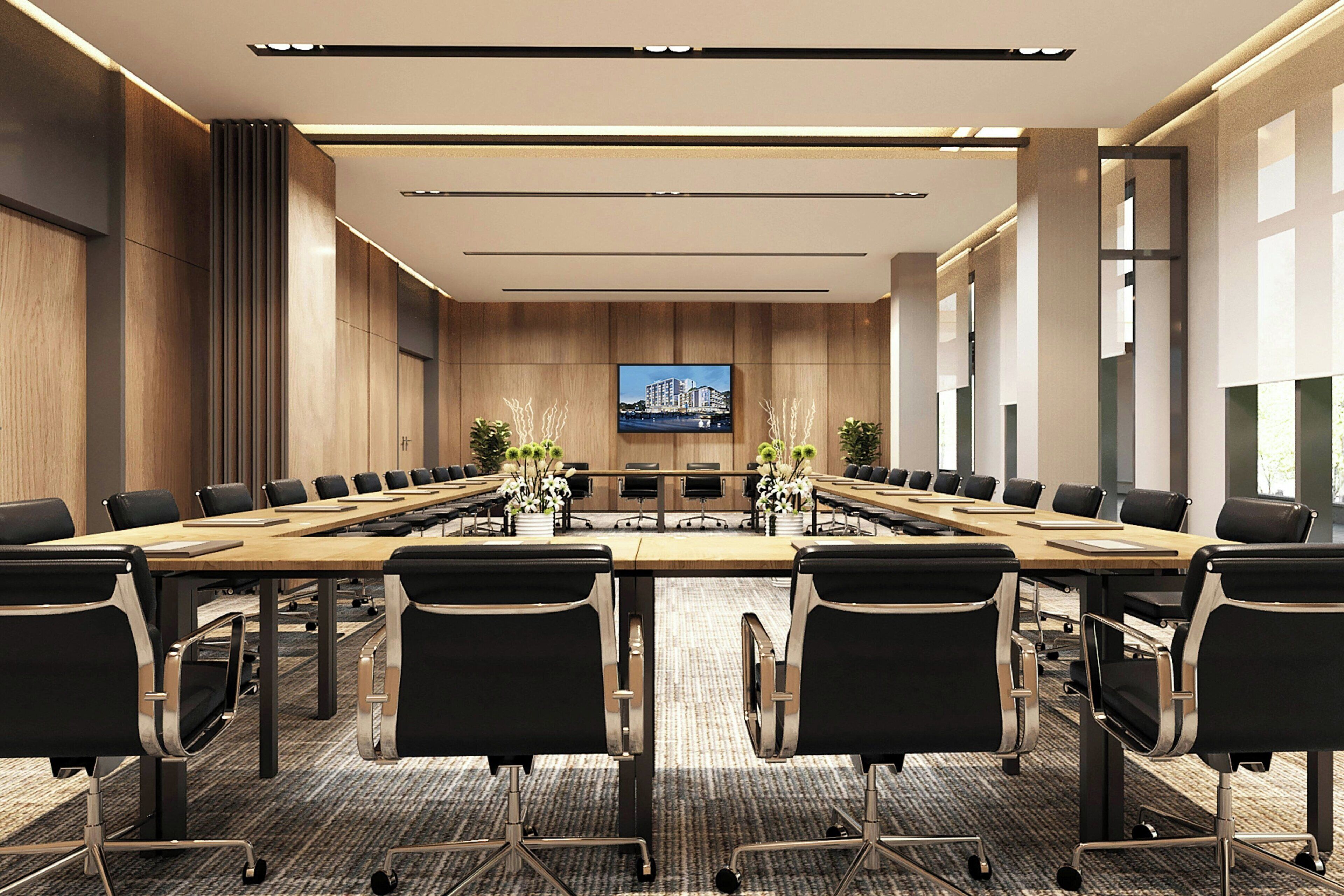 A conference room with a long table, black chairs, and a television screen on the wall.