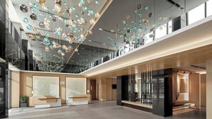 A spacious lobby with a modern design, featuring a suspended light fixture and a reception desk.