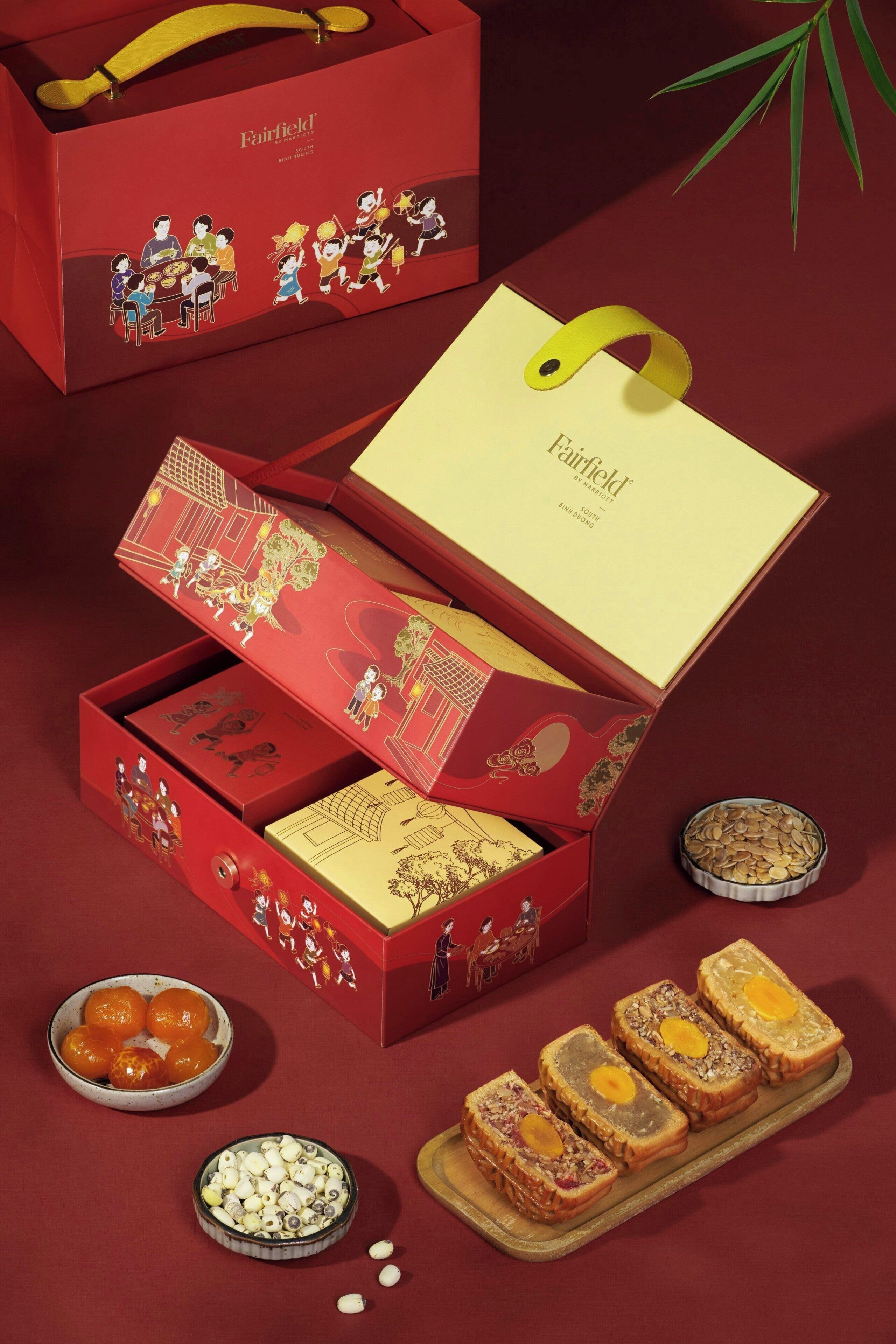 Una caja roja con asa amarilla, que contiene diversos alimentos y una tarjeta con el logo de Fairfield by Marriott.