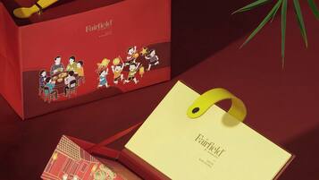 Una caja roja con asa amarilla, que contiene diversos alimentos y una tarjeta con el logo de Fairfield by Marriott.