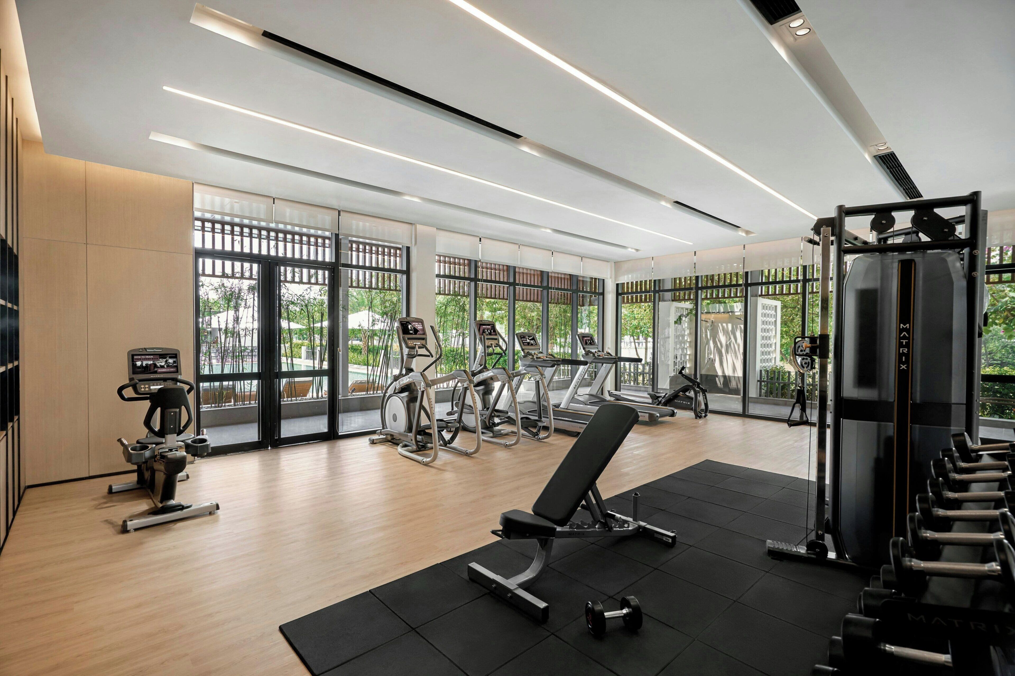 A modern gym with cardio machines, free weights, and a bench.