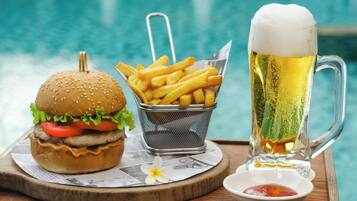 Un plateau repas avec un hamburger, des frites et une chope de bière, posé près d’une piscine.