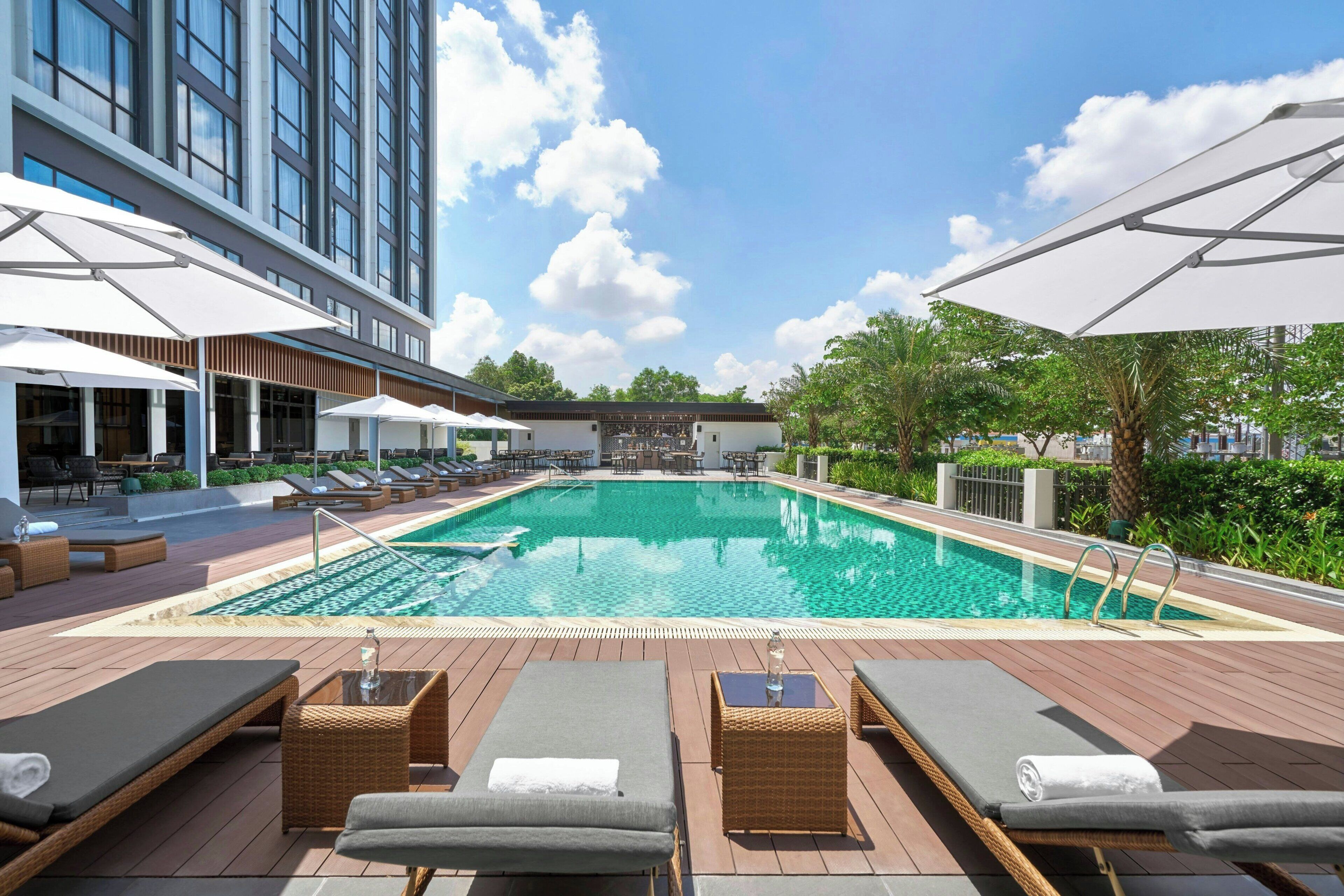 A rooftop pool area with lounge chairs, umbrellas, and a clear view of the sky.