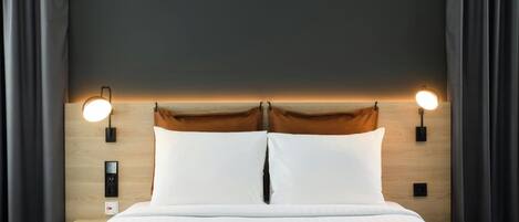 A neatly made bed with white linens, two wall-mounted reading lights, and a wooden headboard.