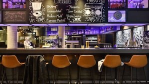 Zona de bar con un menú en pizarra que enumera cócteles, una barra y taburetes naranjas.