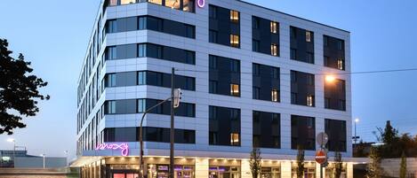 A modern hotel with a prominent neon sign, multiple floors, and a well-lit entrance.