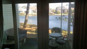 A room with a sliding glass door leading to a view of a body of water, a small table with chairs, and a wicker chair. - 3 Bedrm, 2 Bath Ground-floor Lake-side, 5 min walk to beach. Great for families! (North Myrtle Beach)