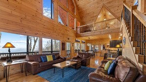 A spacious wooden interior with a high ceiling, a staircase, and a view through large windows. - Cabin in the Clouds, Best Views, Hot Tub, Games, Firepit, Pets, Flat Paved Drive (Mineral Bluff)