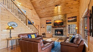 A wooden cabin interior with a fireplace, leather sofas, a staircase, and a welcome sign. - Cabin in the Clouds, Best Views, Hot Tub, Games, Firepit, Pets, Flat Paved Drive (Mineral Bluff)
