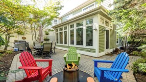 Een terras met buitenmeubilair, een vuurkorf en een huis op de achtergrond.