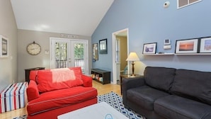 A living room with a red sofa, a black sofa, and a patterned rug. There is a door labeled "LIFES A BEACH" and a wall with framed pictures. - Union Pier Home With Hot Tub and One Block To Beach! (Union Pier)