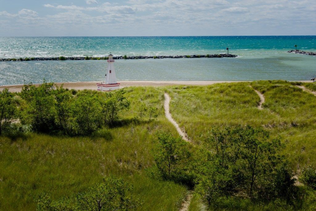 A lighthouse on a grassy hill overlooking a beach with a clear view of the ocean.