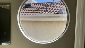 A bathroom with a round window, a mirror, and a toilet paper holder.
