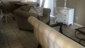 A living room with a sofa, a coffee table, a lamp, and a window with curtains.