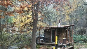 A rustic cabin with a wooden deck, surrounded by autumn foliage. - French Creek Inn.    Creekside Cabin with Fire Sauna (Riggins)