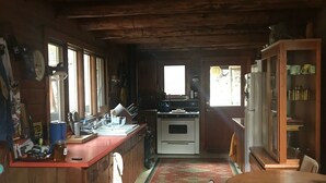 A rustic cabin interior with a wooden dining table, a kitchen area with a refrigerator and stove, and a patterned rug on the floor. - French Creek Inn.    Creekside Cabin with Fire Sauna (Riggins)