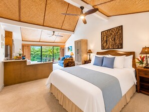 A hotel room with a large bed, a balcony with a view, a ceiling fan, and a wooden headboard.