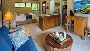 Amplia sala de estar con techo alto, ventilador de techo, sofá, mesa de centro, zona de cocina con refrigerador y un gran ventanal con vistas al exterior.