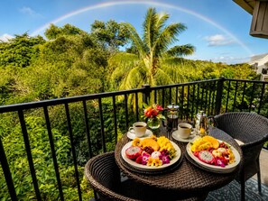 A balcony with wicker furniture, a table set with breakfast, and a lush tropical background.