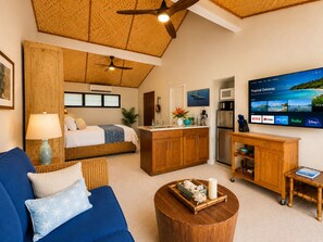 A compact living space with a bed, sofa, kitchenette, and a television displaying a tropical getaway. - Princeville AC + Purple King Top-Floor Tiki Suite, Near 1 Hotel & Beaches (Princeville)