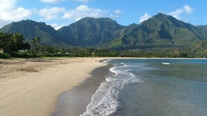 Una playa con montañas al fondo, cielos despejados y aguas tranquilas.
