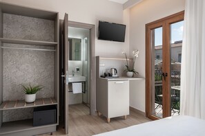 A modern hotel room with a bed, a desk, a TV, a bathroom with a sink and mirror, and a balcony with outdoor furniture. - Al Daliani Minaret Rooms (Chania)