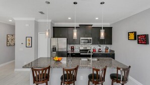 Une cuisine moderne dotée de plans de travail en granit, de meubles sombres, d’appareils électroménagers en acier inoxydable et de luminaires suspendus.