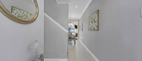 A hallway with a glass table, a decorative lamp, and a mirror on the left wall.