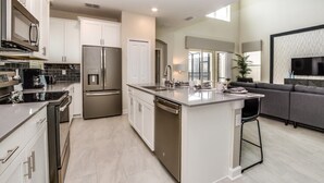 A modern kitchen with stainless steel appliances, a central island, and a grey sofa in the living area.