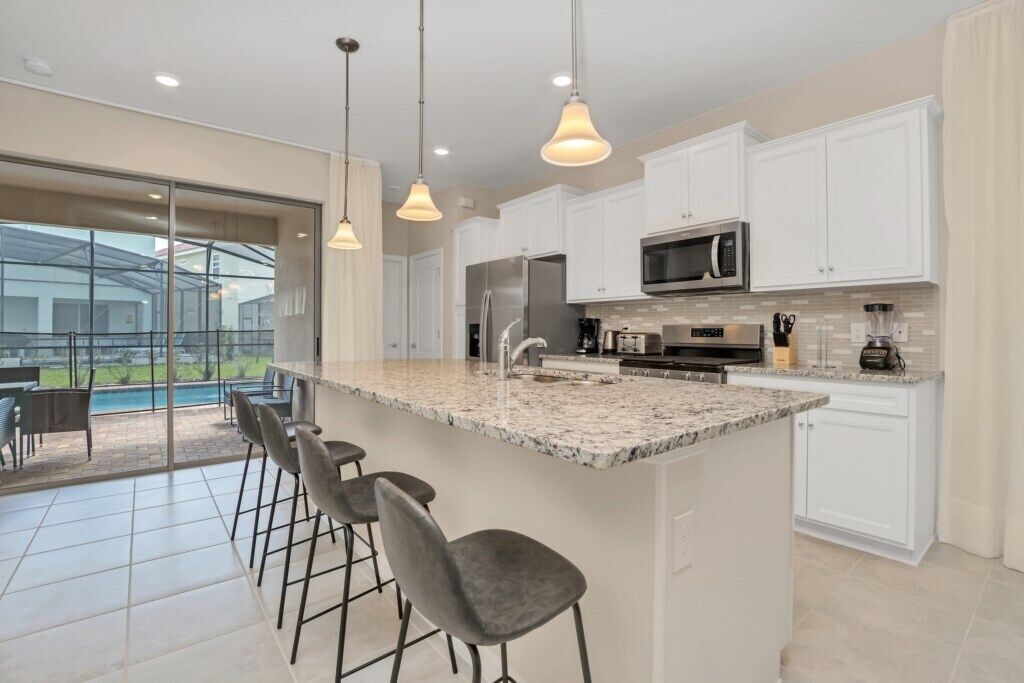 A modern kitchen with white cabinets, a granite countertop, and a bar area with stools.
