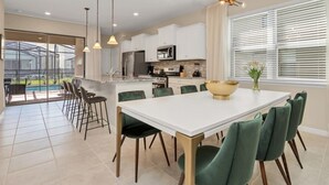 Una cocina moderna con armarios blancos, una isla grande y una zona de comedor con sillas verdes.