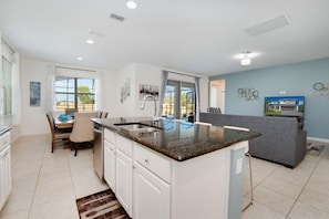 Enjoy meals in the spacious kitchen with a central island and oven, adjacent to a dining area with a wooden table.
