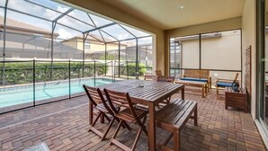 A covered patio with a pool, wooden furniture, and a view of neighboring houses. - Ultimate 8 Bedroom 6 Bathroom Windsor At Westside Resort Villa (Kissimmee)