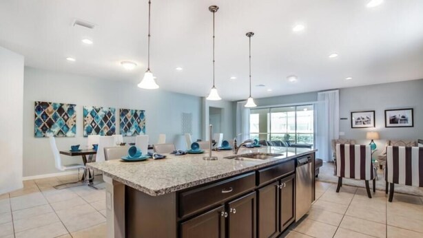 A modern kitchen with a large island, pendant lights, and a dining area with striped chairs. - Ultimate 8 Bedroom 6 Bathroom Windsor At Westside Resort Villa (Kissimmee)
