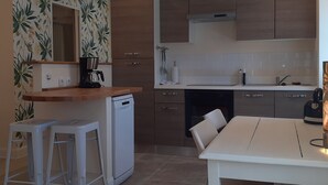 Una cocina funcional con cafetera, lavavajillas y un comedor con mesa y dos taburetes.