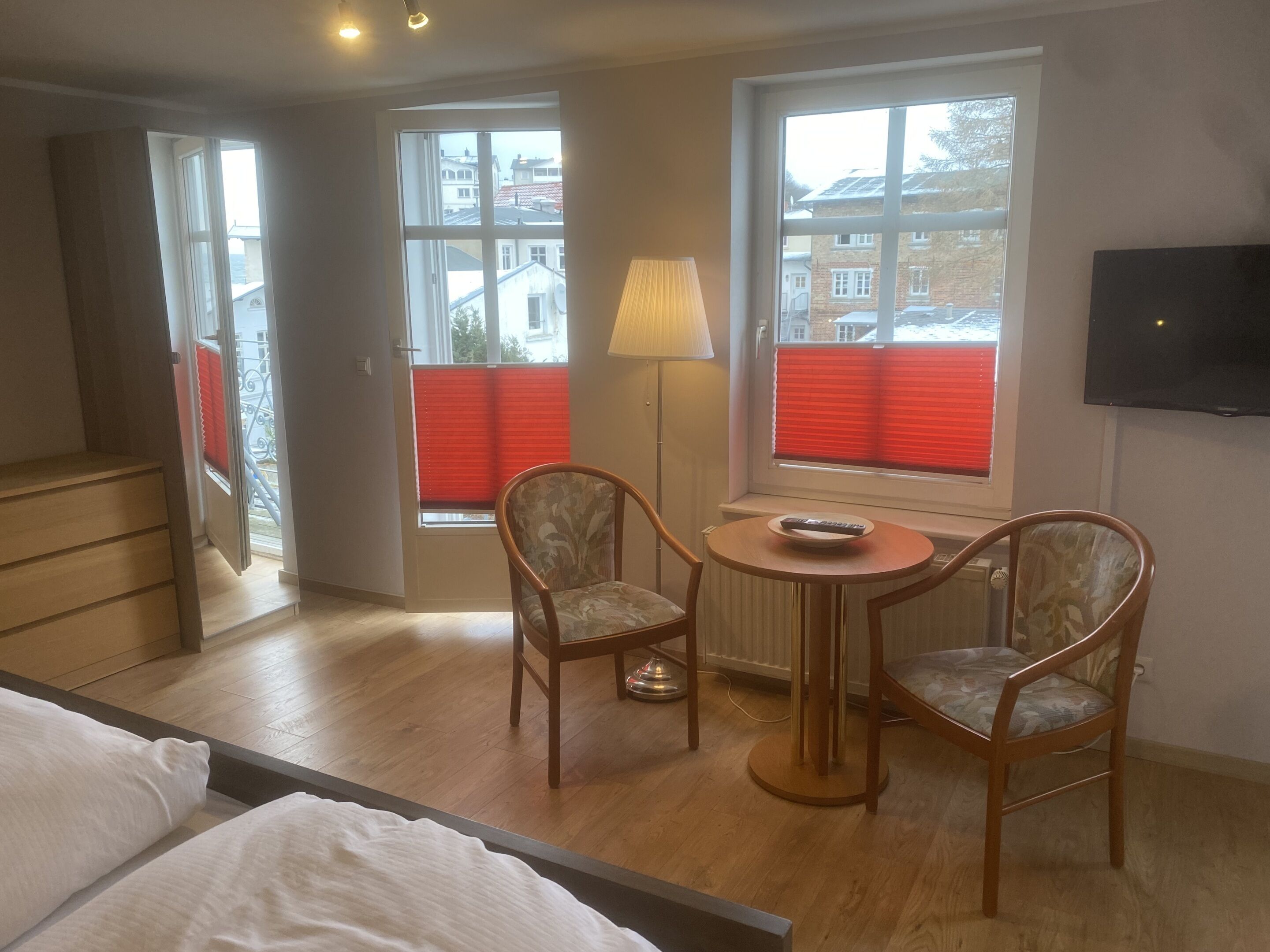 A hotel room with a bed, a small table with chairs, a lamp, and a TV on the wall.