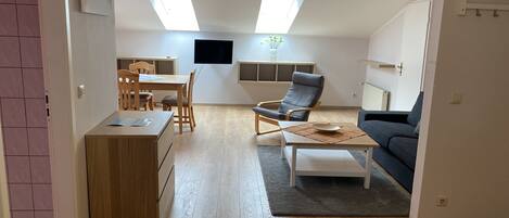A modern living room with a dining area, a grey sofa, a wooden coffee table, and a TV mounted on the wall.