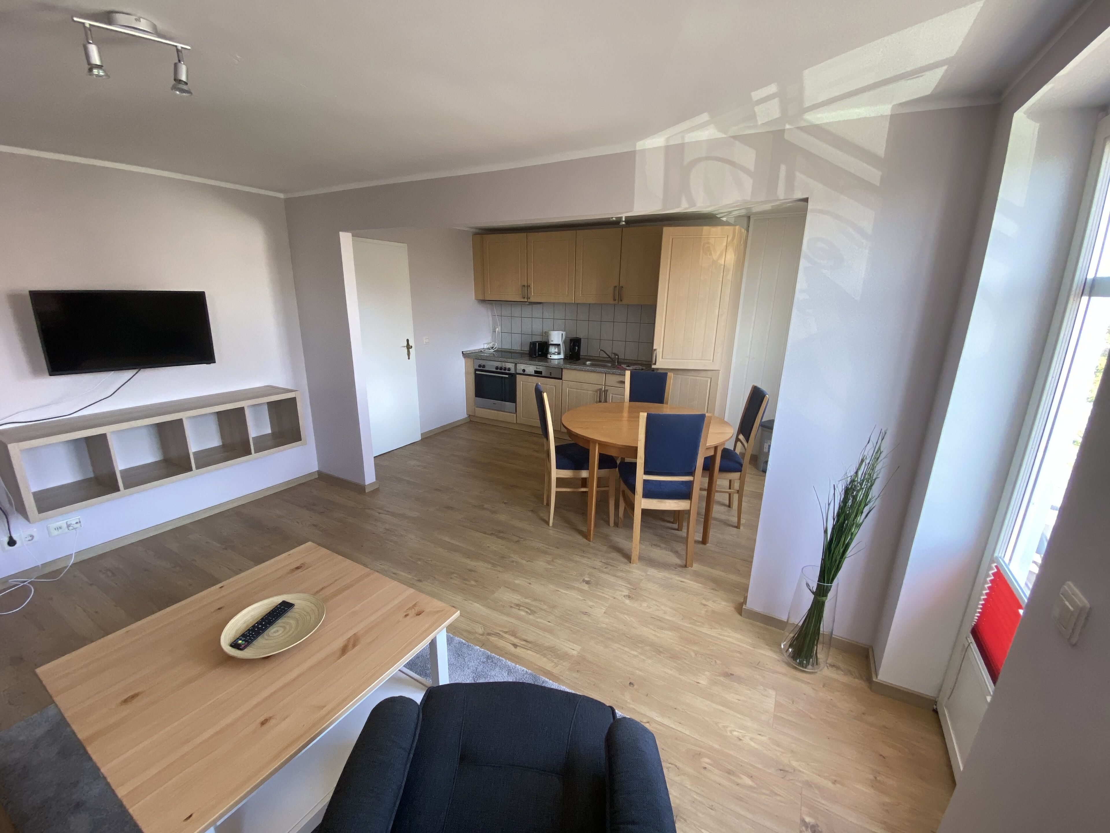 Een moderne woonkamer met een televisie, een houten entertainmentkast en een eethoek met een tafel en stoelen.