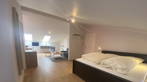 Une chambre avec un grand lit, un bureau et une chaise. Il y a une fenêtre donnant sur l’extérieur.