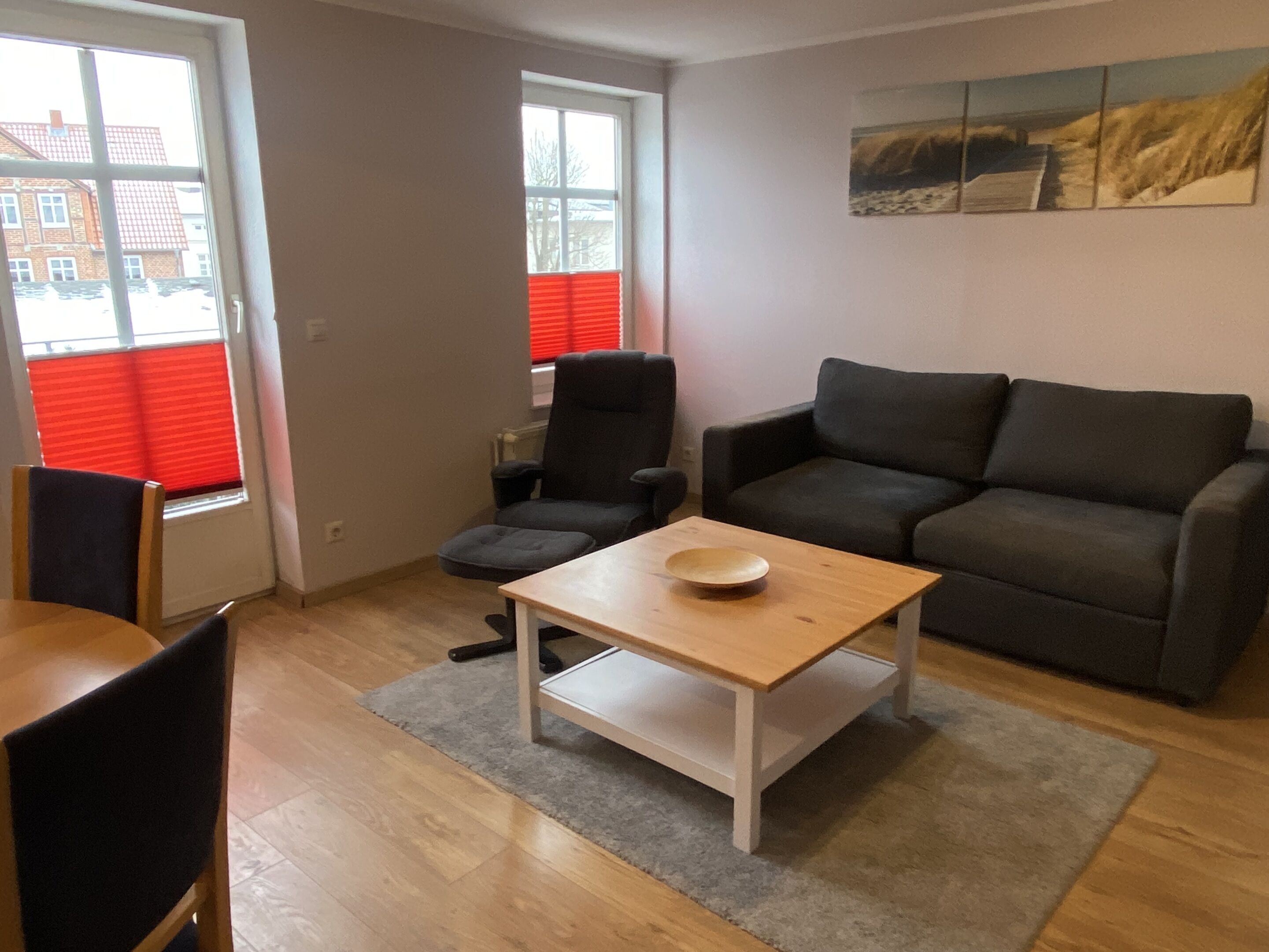 Een woonkamer met een bank, een tafel, een stoel en een raam met zonwering.